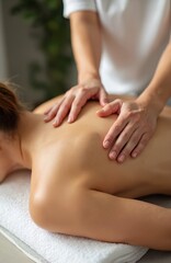 Pro massage therapist works on female patient back muscles. Gentle hands apply therapeutic pressure to shoulder, neck area. Client relaxes on massage table in calm salon environment, promoting