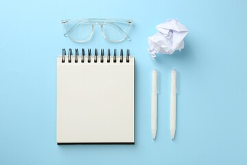 Notebook, glasses, crumpled paper and pens a on light blue background, flat lay