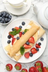 Tasty crepes with cream, berries and mint on white marble table, flat lay