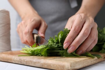 Woman cutting fresh cilantro at white table, closeup