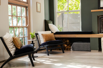 Black wooden lounge chairs featuring white cushions facing bench storing firewood beneath window