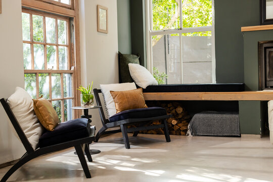 Black wooden lounge chairs featuring white cushions facing bench storing firewood beneath window