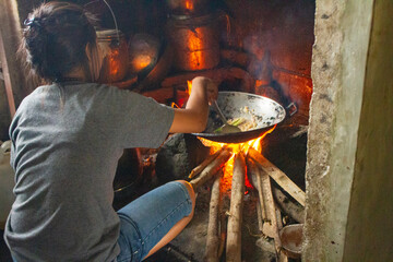 Flores, Indonesia – 07. 14. 2019 - A mother is cooking in the kitchen, using a stove and firewood...