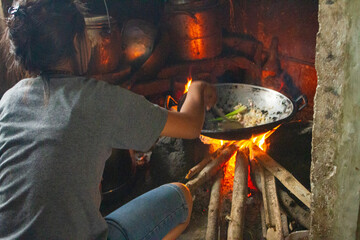 Flores, Indonesia – 07. 14. 2019 - A mother is cooking in the kitchen, using a stove and firewood...