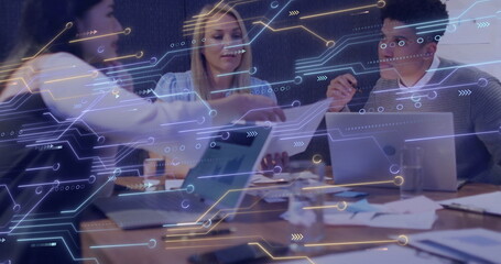 Professionals in office attire collaborating over devices and charts at office table, tech overlay