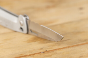 Silver folding knife extended on wood surface, knife concept