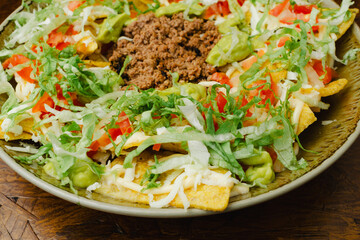 Overhead Shot of Traditional Mexican Chilaquiles with Ground Beef, Guacamole, Lettuce, Tomato and Cheese on a Rustic Wooden Table