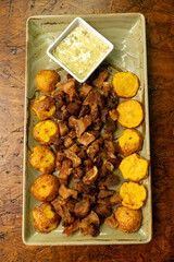 Overhead Shot of Colombian-Style Crispy Pork Belly (Chicharrón) with Golden Potatoes and Creamy Sauce on Rustic Ceramic Plate