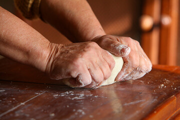 closeup of hands of elderly woman , casually dressed at home, making dough by hand on  a simple  wooden rustic table