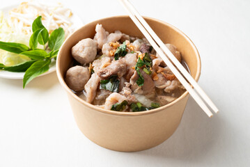 Thai noodles soup with sliced pork, minced pork, meatball and liver in a kraft paper bowl eating with fresh vegetables on white background, Traditional Thai street food