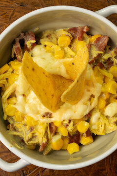 Traditional Colombian Mazorcada or Desgranado in a bowl, a comforting street food dish with sweet corn, shredded chicken, bacon, and melted cheese, garnished with nachos and served on a wooden table.