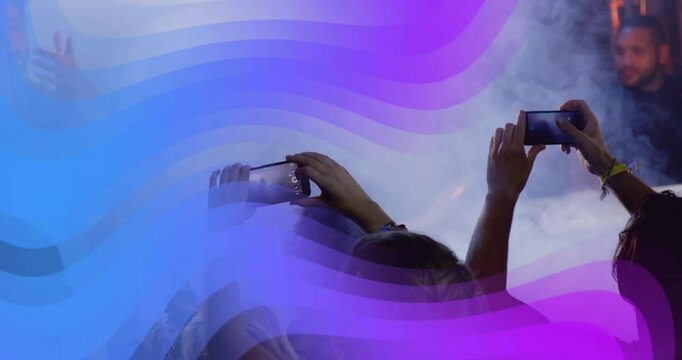 Front row fan lifting phone to record sparking light waves sweeping highlighting singer at concert