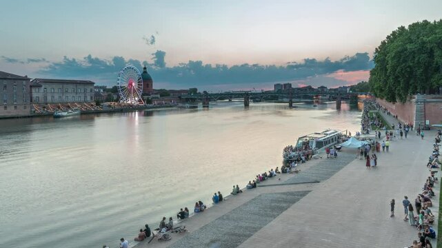 Aerial view of Port de la Daurade park along the Garonne River day to night transition timelapse in Toulouse, France. La Grave Hospital with Saint-Pierre Bridge during sunset with colorful clouds