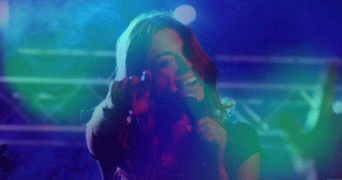 Female singer stepping into beam at music venue, singing and engaging crowd amid pulsing haze