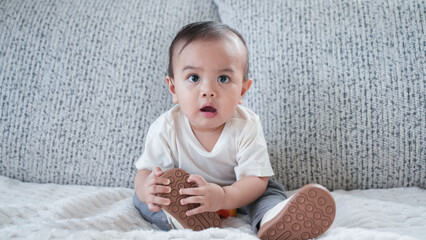 Adorable baby boy playing and crawling on a cozy couch in a bright living room at home.