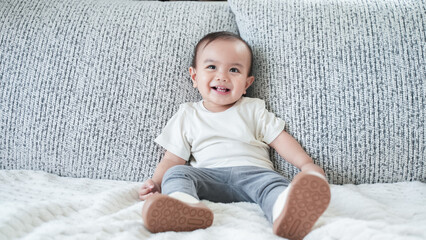 Adorable baby boy playing and crawling on a cozy couch in a bright living room at home.