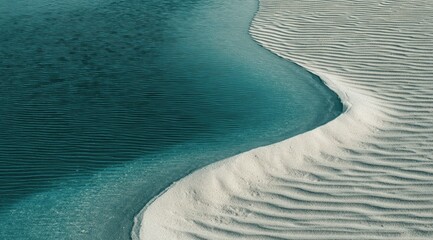 Teal water gently curves into a pale sand dune, creating an abstract, flowing landscape.  The texture of the sand is visible, showing subtle ripples