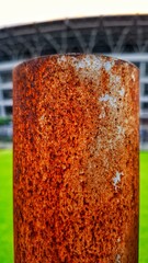 A rusted iron pole with green grass in the background. The texture of the rust on the iron peeling...