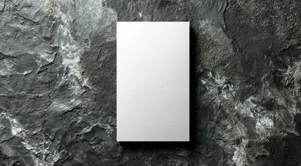 A clean, white rectangular card rests on a dark, textured stone background.  The card is vertically oriented and slightly shadowed, enhancing its three-dimensionality against the rough surface