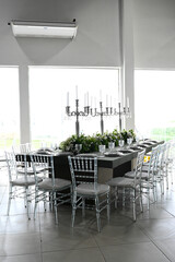 table set in ballroom, elegant wedding reception table with candlesticks, luxury dinner arrangement with floral centerpiece, formal dining table with clear chairs and silver candelabras
