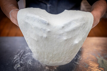 Quito, Ecuador - June 14, 2025: Floured hands mixing ingredients that shape the pizza dough. A...