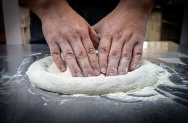 Quito, Ecuador - June 14, 2025: Floured hands mixing ingredients that shape the pizza dough. A...