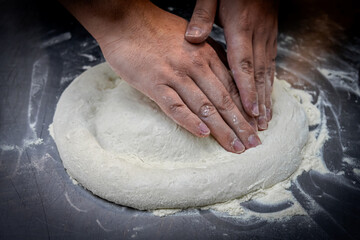 Quito, Ecuador - June 14, 2025: Floured hands mixing ingredients that shape the pizza dough. A...
