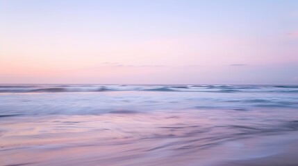 Fototapeta premium Soft pastel sunset painting the sky over a calm ocean beach, with gentle waves lapping the shore. The sky blends hues of pink, blue, and purple, while the water mirrors the serene colors, 