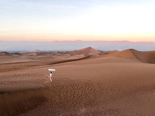 Woman in bright coloured clothes standing in desert on dunes and holding sand board over the head after sledding down on sand. Tourist is kicking the sand up and having a fun during traveling in Peru,