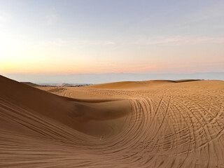 Photo of desert at sunrise sunset hour with dune buggy tires tracks in the sand. Buggy tours as a one of tourist attraction  in Huacachina, Ica, Peru. Extreme sports, adventure, journey and travel.