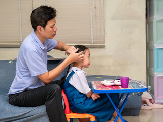Father does his little daughter's hair in the living room in the morning before she goes to school.