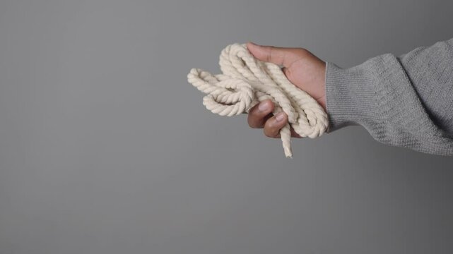 A hand firmly grips a coiled rope against a gray backdrop