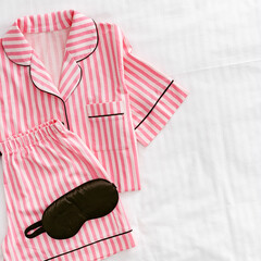 Pink white Pajama Set with black silk sleep mask on white sheet. Top view layout fashion woman home...
