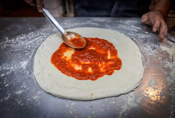 Gently adding tomato sauce with a spoon to the pizza dough, infusing it with flavor and color. A...