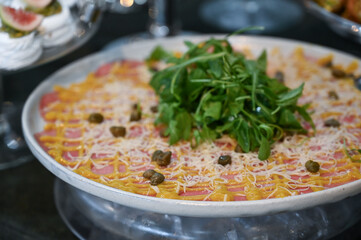 carpaccio , thin beef carpaccio with arugula and parmesan, gourmet meat appetizer with vinaigrette topping, elegant carpaccio platter served cold for events	