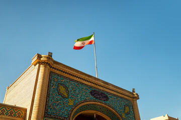 Iranian national flag on a flagpole against clear blue sky. Symbol of the Islamic Republic of Iran,...