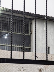 Metal bars in front of a building on a rainy day, with visible raindrops and gray walls.