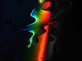 Rainbow is reflected in the water droplets on a dark surface