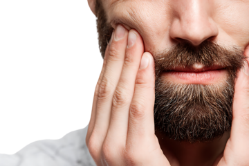 Close up of a man with a beard holding his jaw in pain.