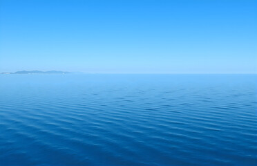 Obraz premium Blue Sea Surface and Distant Mountains