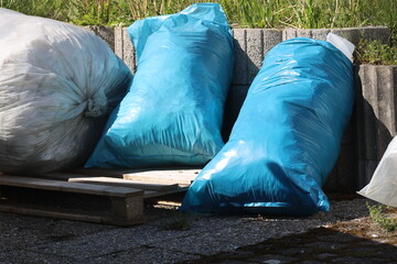 Two blue plastic bags are on the ground next to a pile of white bags