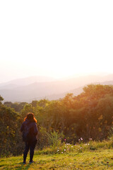 Asian young woman backpack smiling and standing with wildflower and beautiful landscape of valley Doi Luang Chiang Dao mountain, Chiang Mai Province of Thailand 