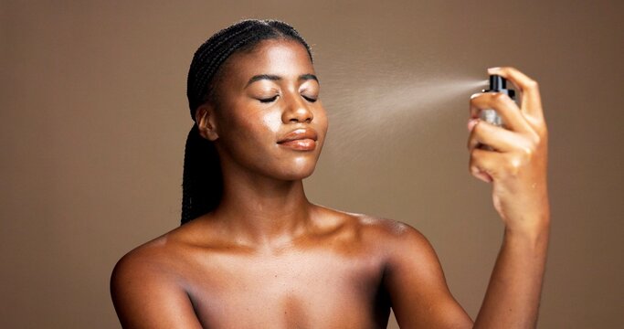 Beauty, cosmetics and setting spray with black woman in studio for facial or makeover product. Face, finishing mist and makeup with African model isolated on brown background for cosmetology