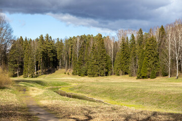 Spring landscape in Pavlovsk Park: Slavyanka River winds through green meadows, edged by spruce and...