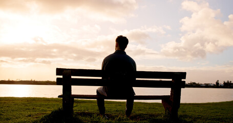 Man, thinking or back view with sunset on bench at lake for daydreaming, memory or break in nature. Male person, relax and fresh air with cloudy sky for rest, contemplating or travel at river or pond