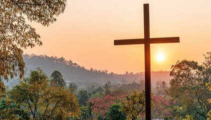 A simple wooden cross against a sunrise over a hilltop landscape