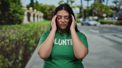 Young plus-size woman in green volunteer shirt standing with eyes closed on a city street looks...