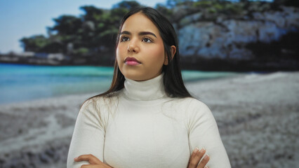 Woman standing with arms crossed on beach as a young latin hispanic figure shows serious expression...