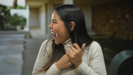 Young woman indoors expressing excitement with her eyes closed and hands near her mouth, captured...