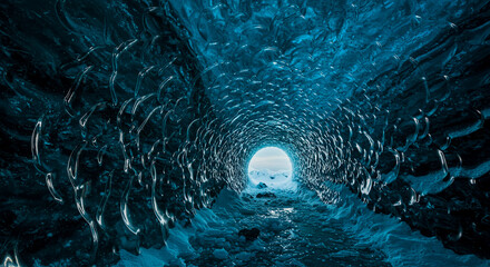 An awe-inspiring view from within a glacial ice cave reveals a frozen tunnel of sculpted blue ice leading towards a bright, distant exit bathed in white light